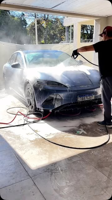 Lavagem técnica em ação, spray de água sobre a lataria em contraluz